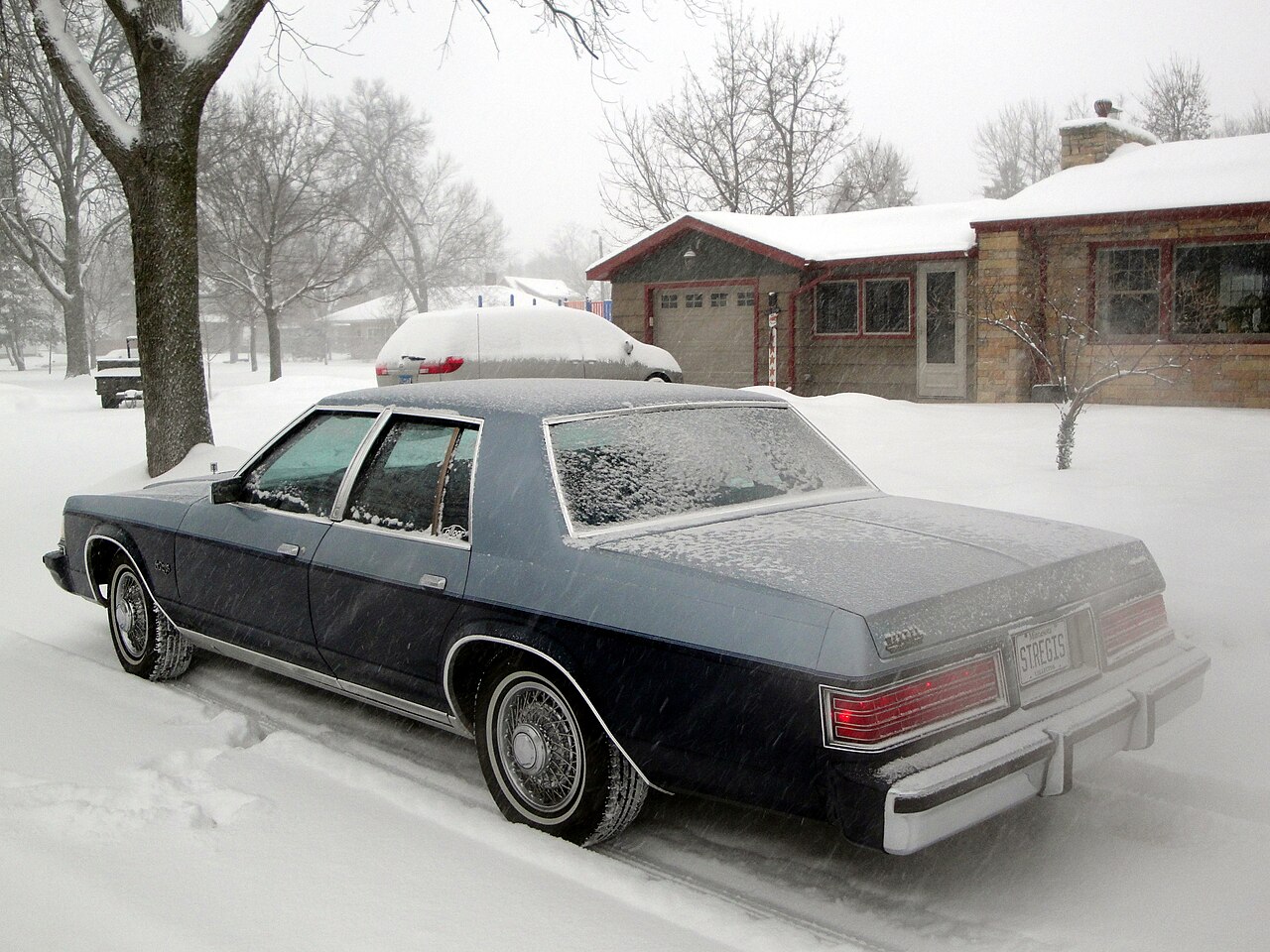 A sedan parked in a snow-covered residential driveway.