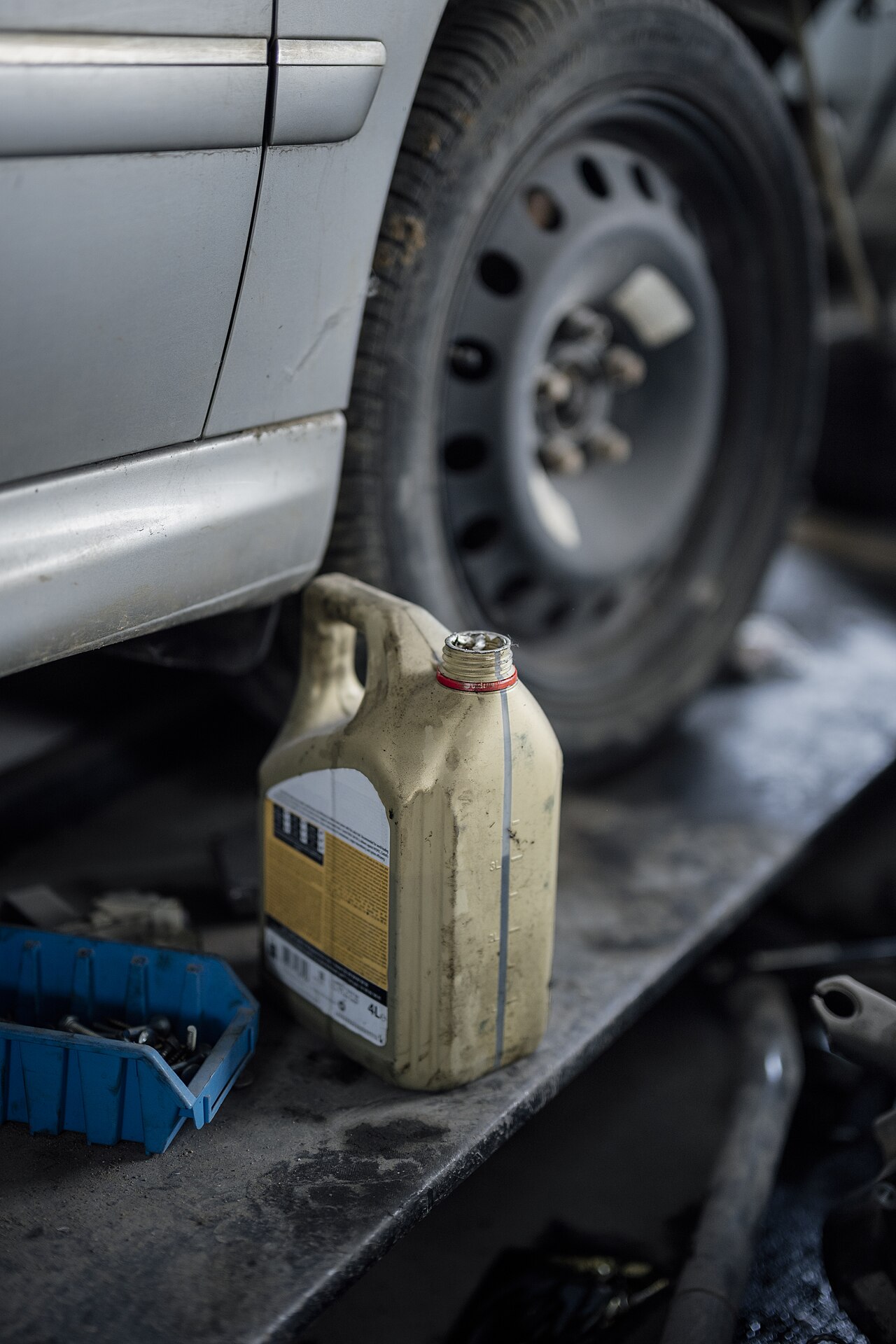 Oil container and tools beside the wheel of a car in a workshop.