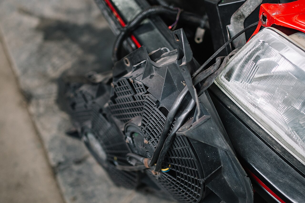 A removed cooling fan beside the front of a vehicle during workshop repairs.