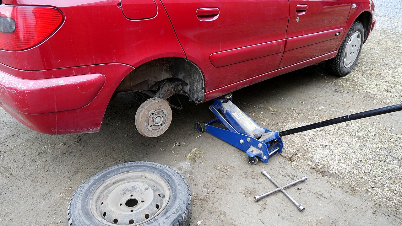 A red parked car during a wheel change with the removed wheel on the ground
