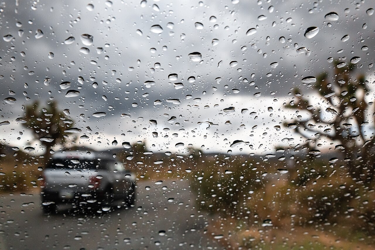 Raindrops on a windshield with another vehicle blurred beyond the glass
