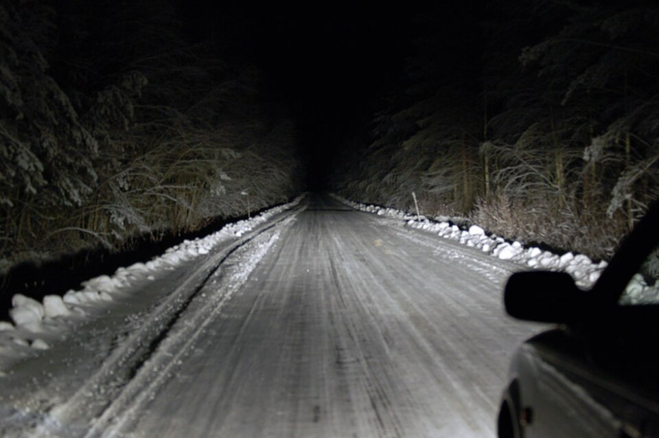A snowy road at night illuminated by a vehicle headlight beam