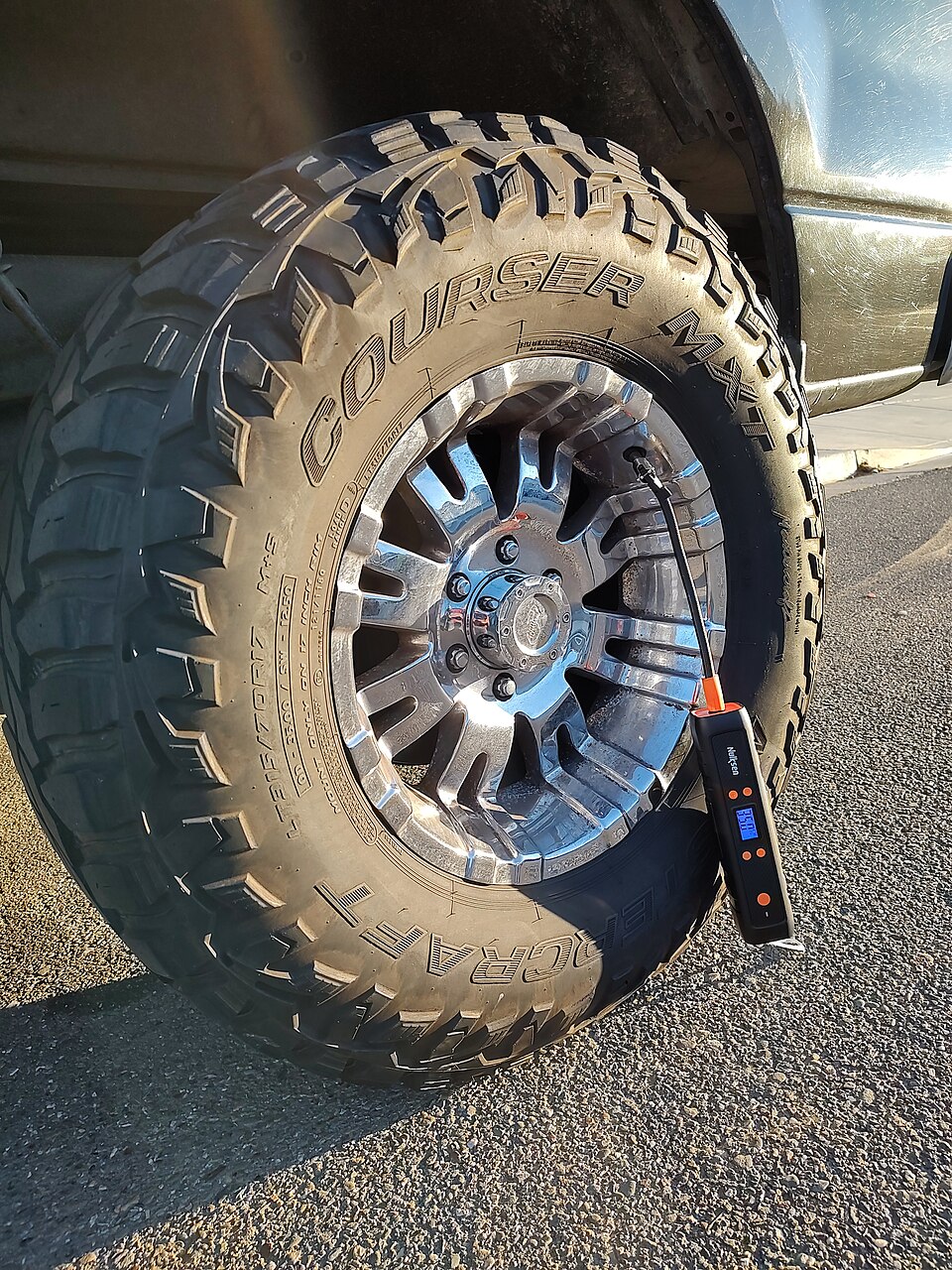 An installed vehicle tire being inflated outdoors. The pictured inflator is neither model compared here; the scene illustrates positioning, not tested suitability.